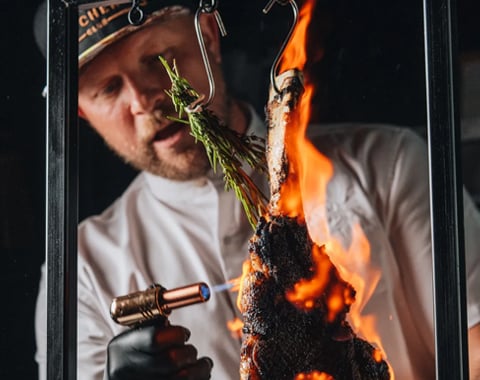 A man torching a piece of tomahawk steak