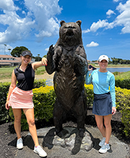 two golfers pose with the bear trap statue